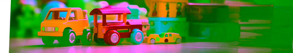 Na zdjęciu widoczne są kolorowe zabawki dziecięce ustawione w rzędzie na drewnianej powierzchni. W centrum kompozycji znajduje się żółta ciężarówka, czerwona lokomotywa z niebieskimi kołami oraz mały żółty samochodzik. W tle można dostrzec kolorowe klocki i inne zabawki edukacyjne w różnych kolorach. Obraz przedstawia przyjazne i stymulujące środowisko terapeutyczne, jakie Poradnia Psychologiczno-Pedagogiczna Expert tworzy podczas warsztatów dla uczniów. Kolorowe zabawki symbolizują różnorodność metod pracy z dziećmi, które poprzez zabawę uczą się ważnych umiejętności społecznych, emocjonalnych i poznawczych, zgodnie z zasadami nowoczesnej pedagogiki stosowanej przez specjalistów Poradni.